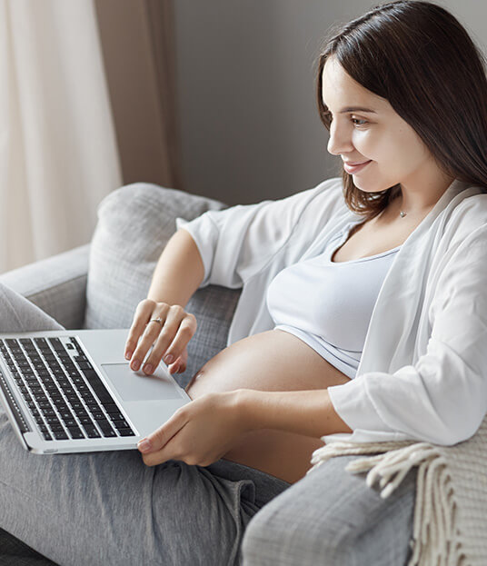 sitting pregnant woman seeking prenatal support on her laptop